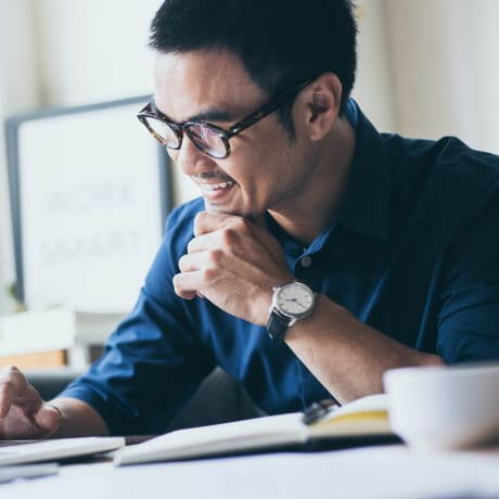 Person wearing glasses in a light, bright office works at a laptop computer.