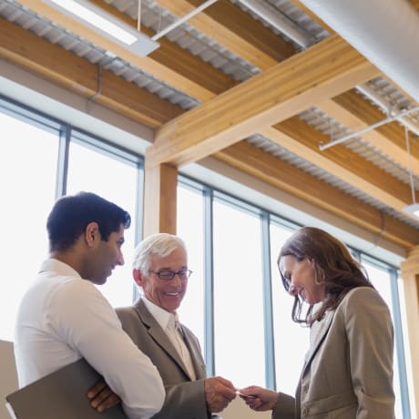 Three people stand in a wood and glass office.