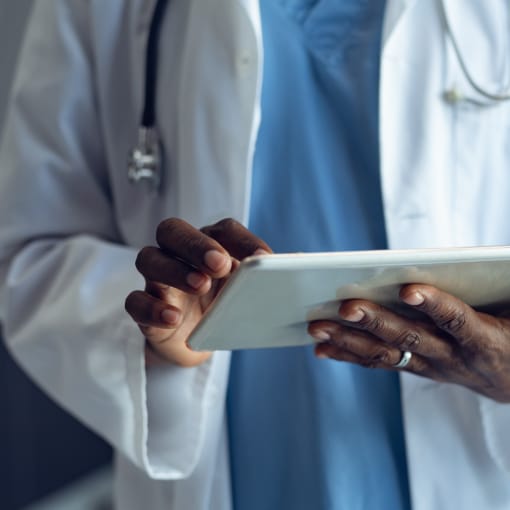 A medical professional wearing a white coat and stethoscope uses a tablet computer.