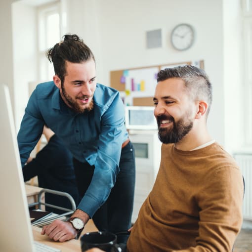 Two people smiling at a monitor while discussing