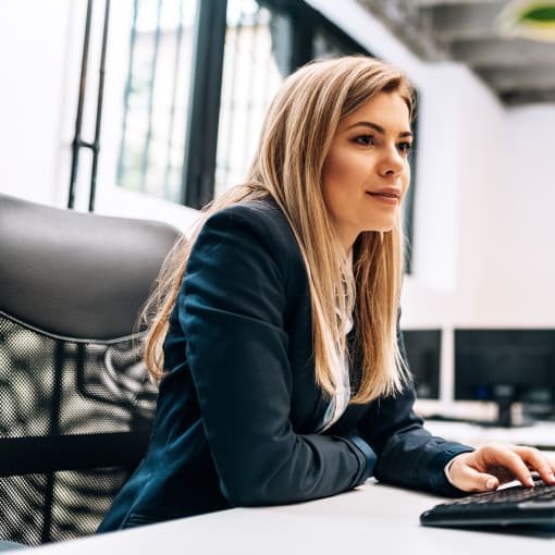 A business professional sits in an office at a dual-monitor desktop computer.