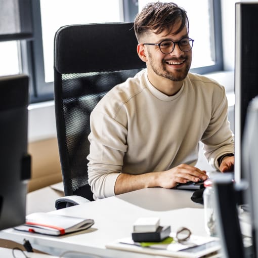 Person sits with multiple desktop computer screens in office setting.