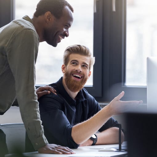 Two colleagues collaborate at a desktop computer in an office.