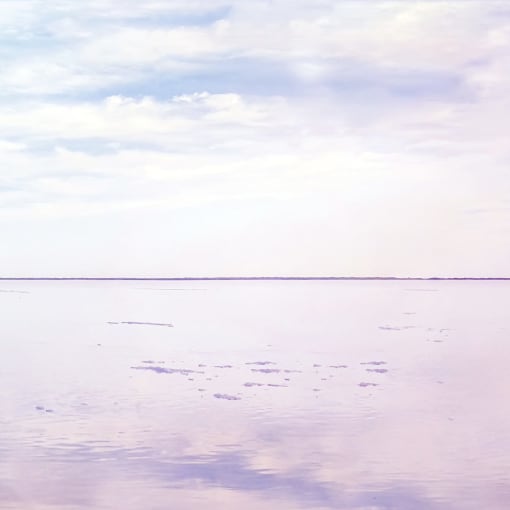 Person stands on reflective ground, looking at blue and pink sky and clouds.