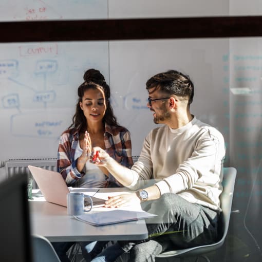 Two people collaborate in a conference room with a whiteboard.