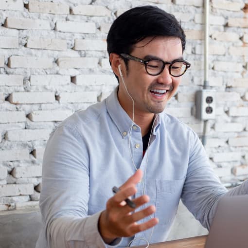 Person in conference call on laptop in front of a white brick wall.