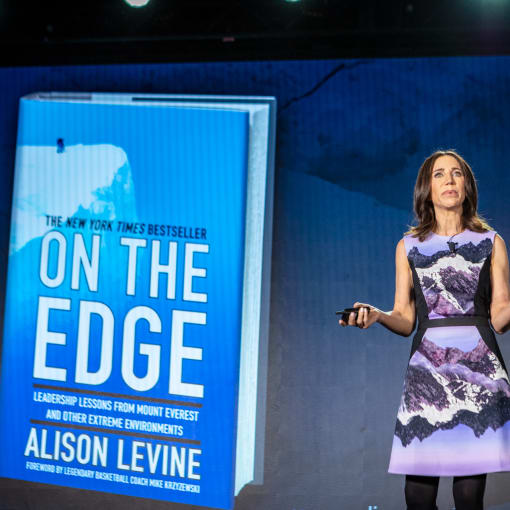 Alison Levine gives speech in purple and black dress in front of a screen showcasing her book, "On the Edge."