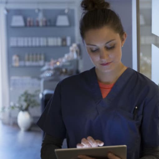 Medical professional wearing scrubs enters data on a tablet computer.