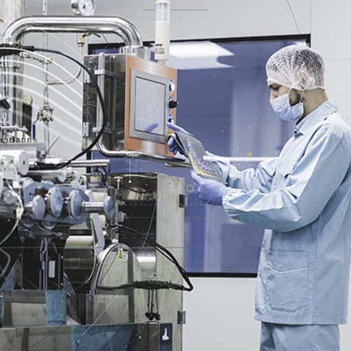 Industrial worker wearing face and head cover works on complex industrial equipment.