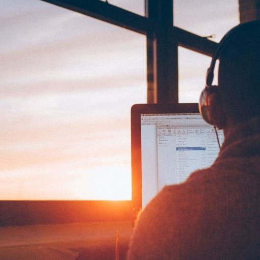 Person wearing headphones works at a computer near a window.