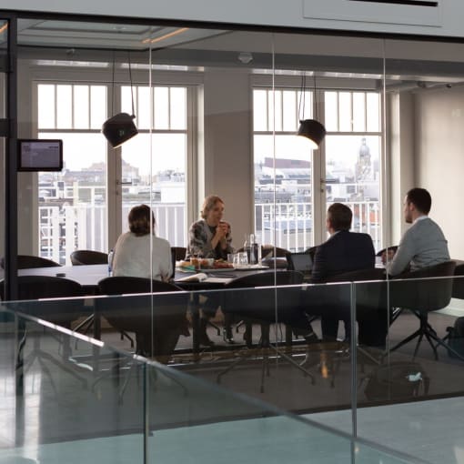 Four people sit in a glass conference room.