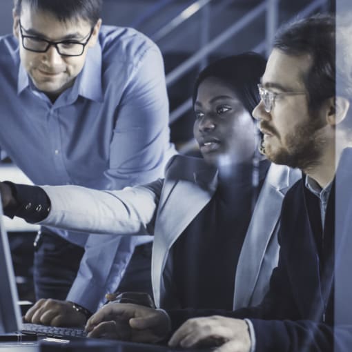 Three people collaborate in front of a desktop computer.