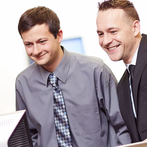 Three people in an office smile at a desktop computer monitor.