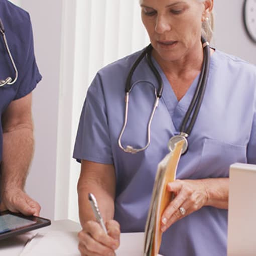 Three medical professionals work using a tablet, physical paper forms, and a desktop computer.