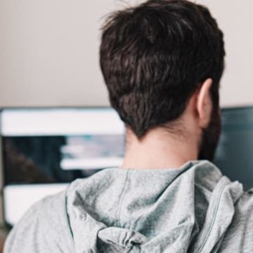 Person wearing hoodie works on dual-monitor desktop computer setup.