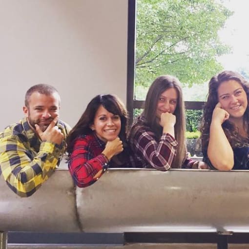 Five people wearing flannel shirts pose while smiling.