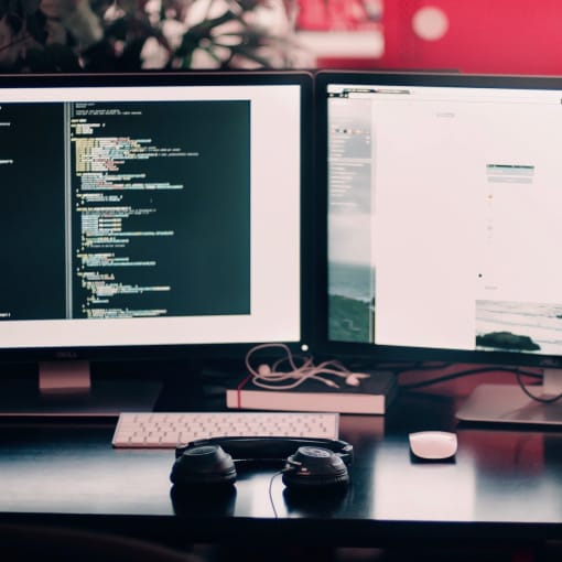 Coding work on a dual-monitor setup on a desk with headphones and cell phone.