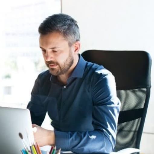 Three people sit in an open office setting, working on computers.