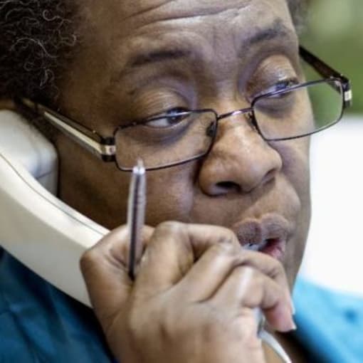 Person in glasses holds a corded phone to their ear.