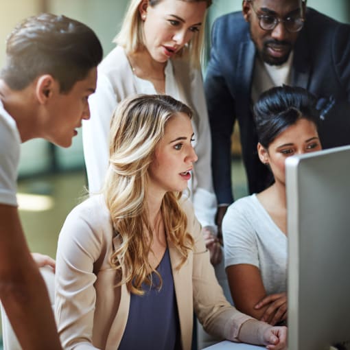 Five people stand around a desktop computer monitor.