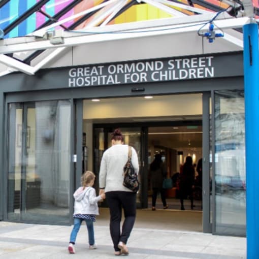 An adult and child walk hand in hand inside Great Ormond Street Hospital for Children.