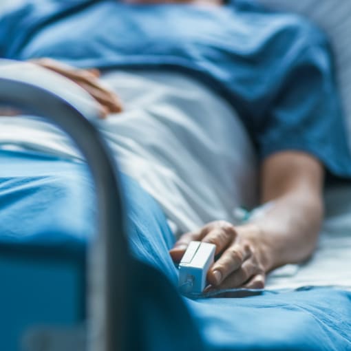 Patient sits in a hospital bed with a finger monitor on.