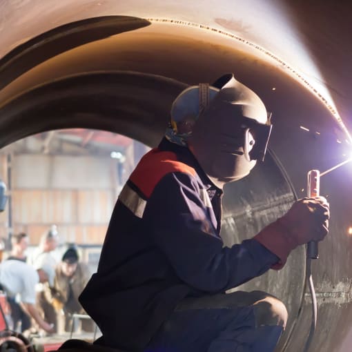 Welder in protective vest and helmet welds metal.