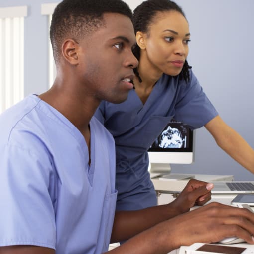 Two medical professionals in scrubs collaborate on medical images on a computer screens.