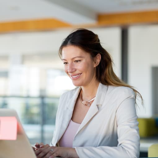 Person in white jacket uses a laptop in a modern office setting.