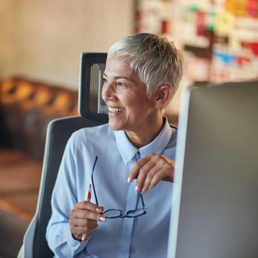 Person in blue button-down shirt sits at a desk in front of a desktop computer.