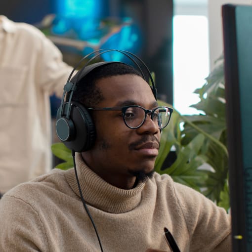 Person wearing headphones and turtleneck sits at a desktop computer.