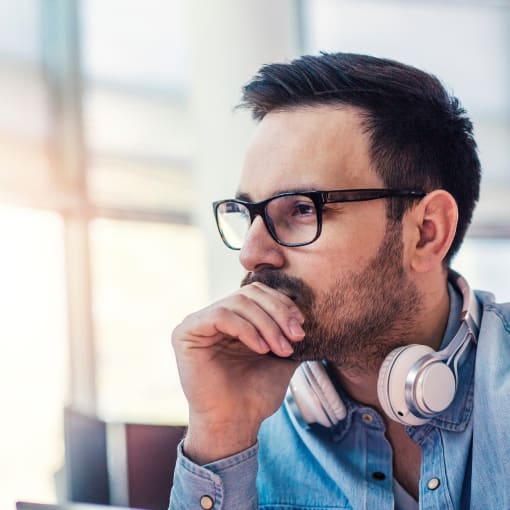 Person with white headphones and holding a tablet computer looks pensive.