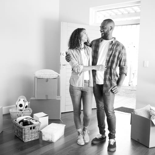 Black-and-white photo of a couple in a barren house with cardboard boxes around them.