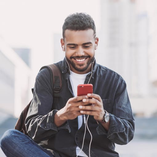 Person in jeans, sneakers and a dark jacket sits outside looking at their phone.