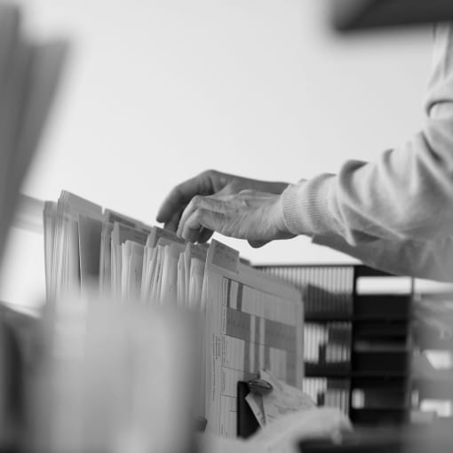 Black and white photo of a person standing at a filing cabinet, rifling through documents.