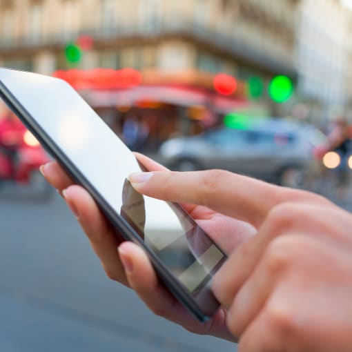 Person holds a mobile phone while walking on a city street.