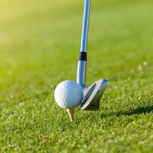 A golf club prepares to hit a ball on a tee.