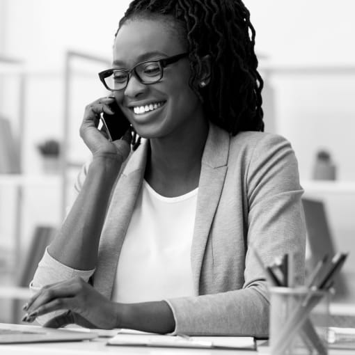 Black-and-white photo of a business professional sitting at a desk with a laptop, pens and small plant.