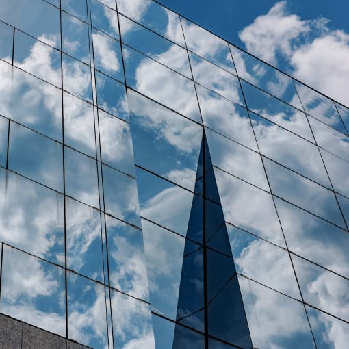 Blue sky and clouds reflected in a building's exterior glass windows.