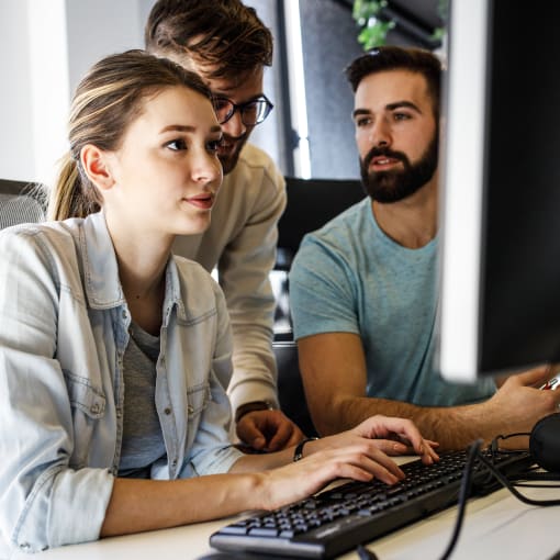 Three people work together at a desktop computer.