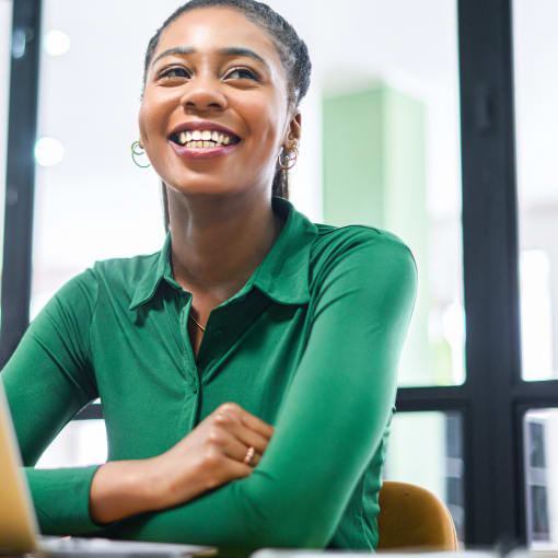 Person in a green blouse smiles while sitting in front of a laptop computer.