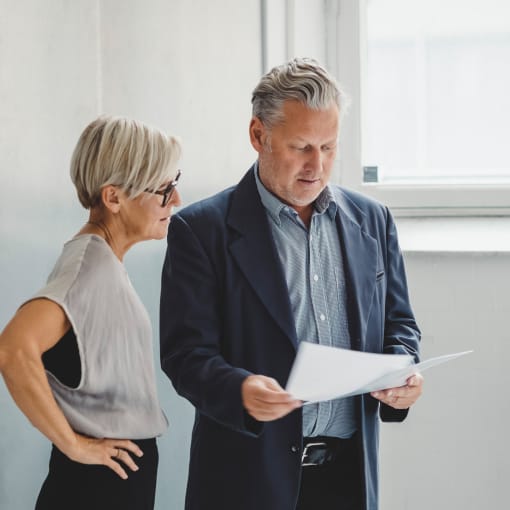 Two people stand in an office and look at paperwork.