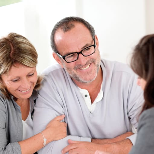 Two people smile and embrace as they look over paperwork with a credit union employee.