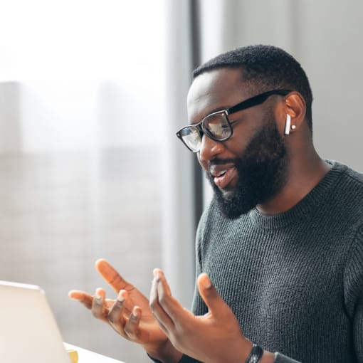 Person sitting in front of a laptop, wearing ear buds and gesticulating.