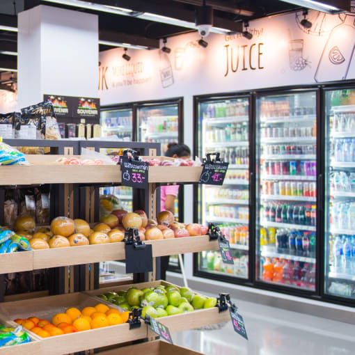 The interior of a convenient store with fresh produce as well as a wall of cold beverages.