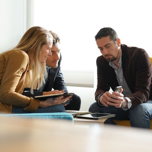 Three people sit and look closely at information on a mobile phone.