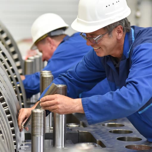 Two industrial workers in hard hats work on turbines.