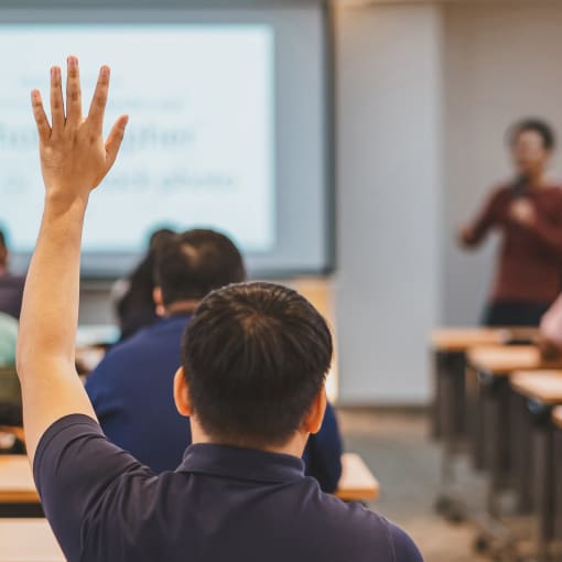 An engaged college or university student raises their hand to ask their professor a question in class.