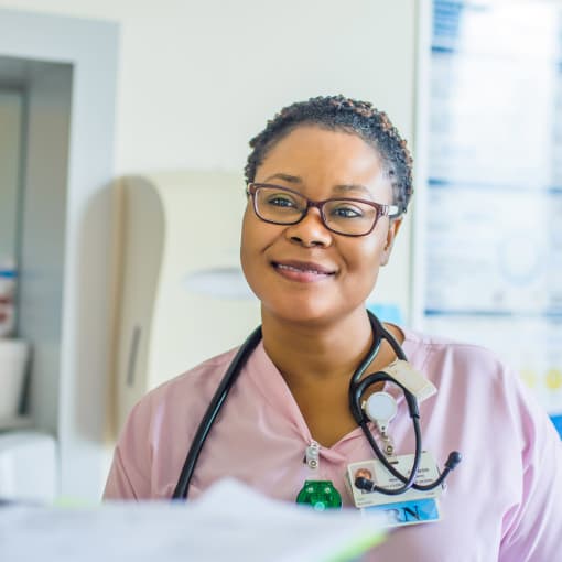 Medical professional wearing pink scrubs and a stethoscope smiles in a healthcare setting.