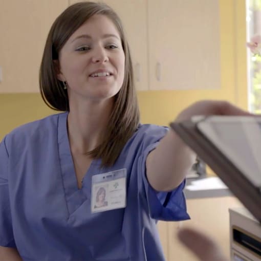 Healthcare professional sits at a reception desk, reaching for forms.